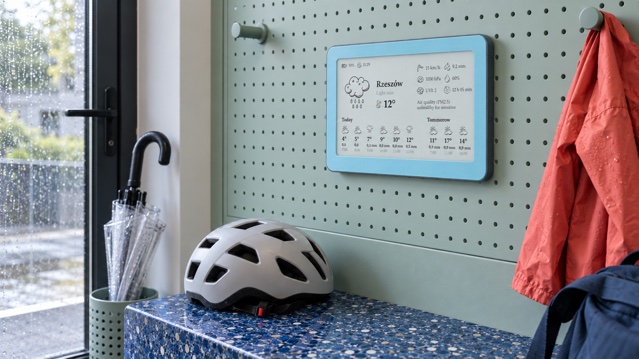 Mist Ice Brisa Daylo på en ljusgrön stålvägg i hallen bredvid regnjacka, paraply och cykelhjälm